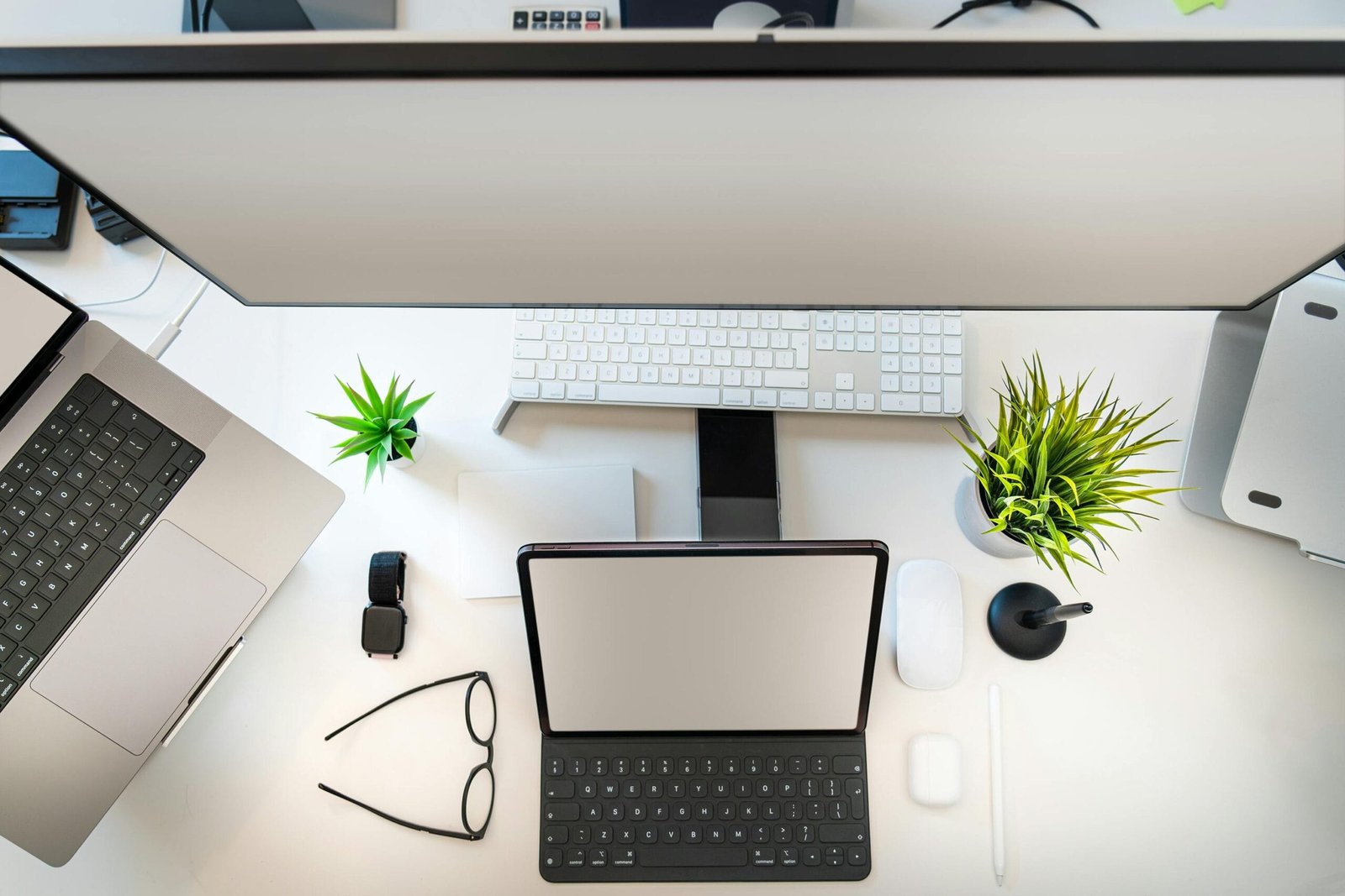 Top view of a minimalist workspace setup with laptop, tablet, and greenery.