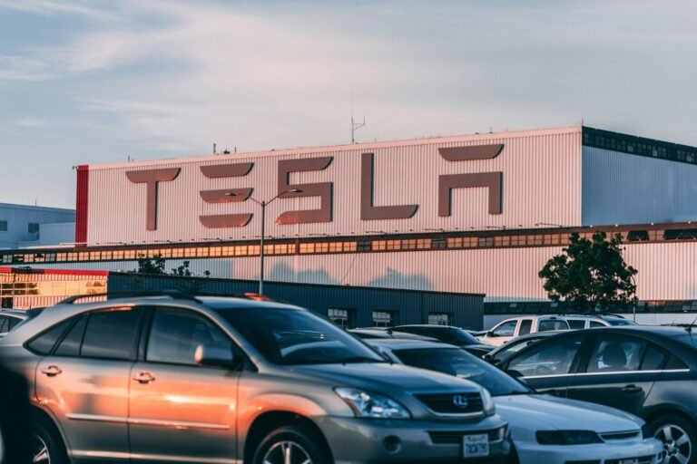 Tesla factory with parked cars during sunset, showcasing modern automotive industry vibes.