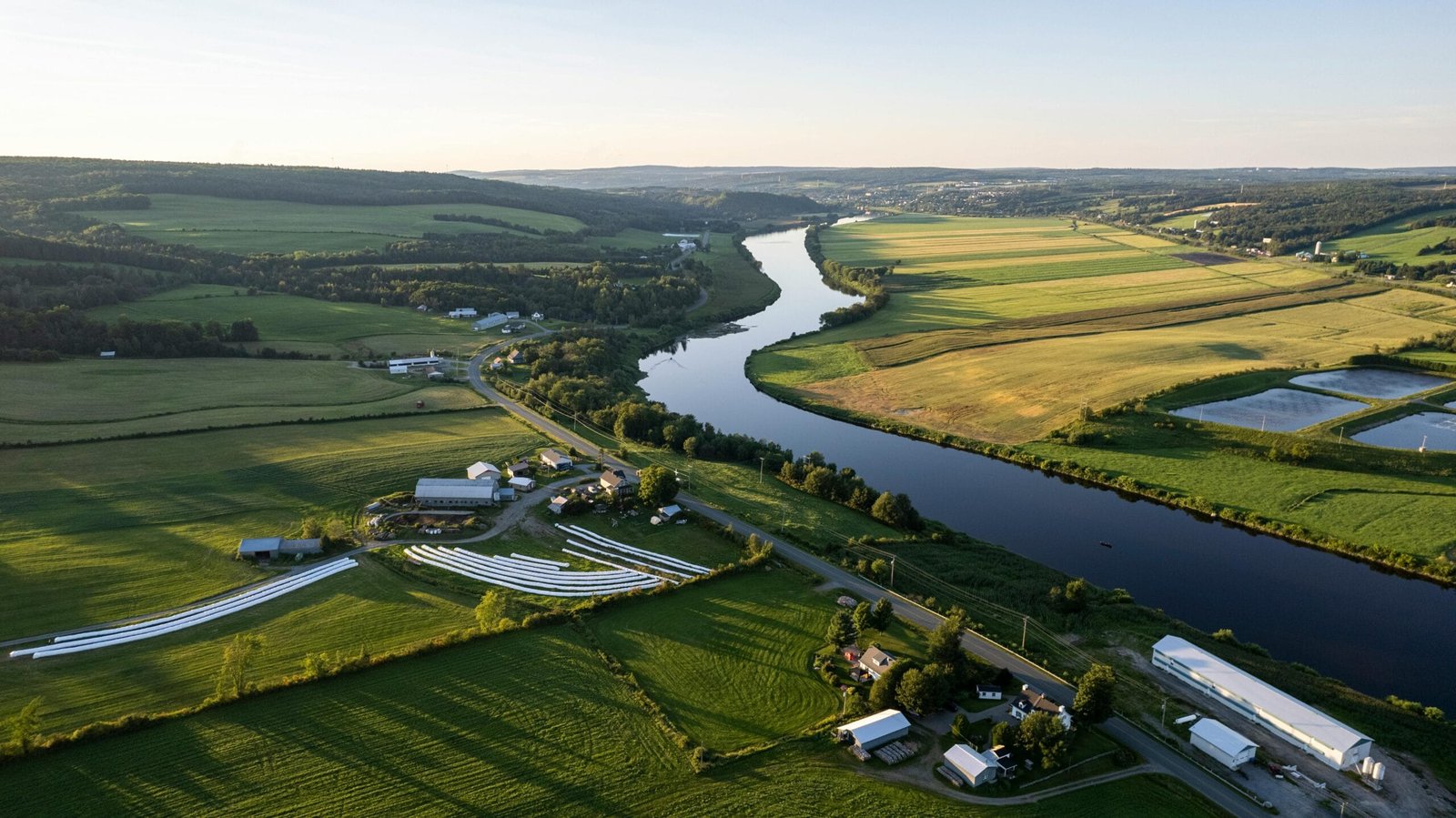 Drone capture of Quebec's picturesque farmland along a winding river at sunset.