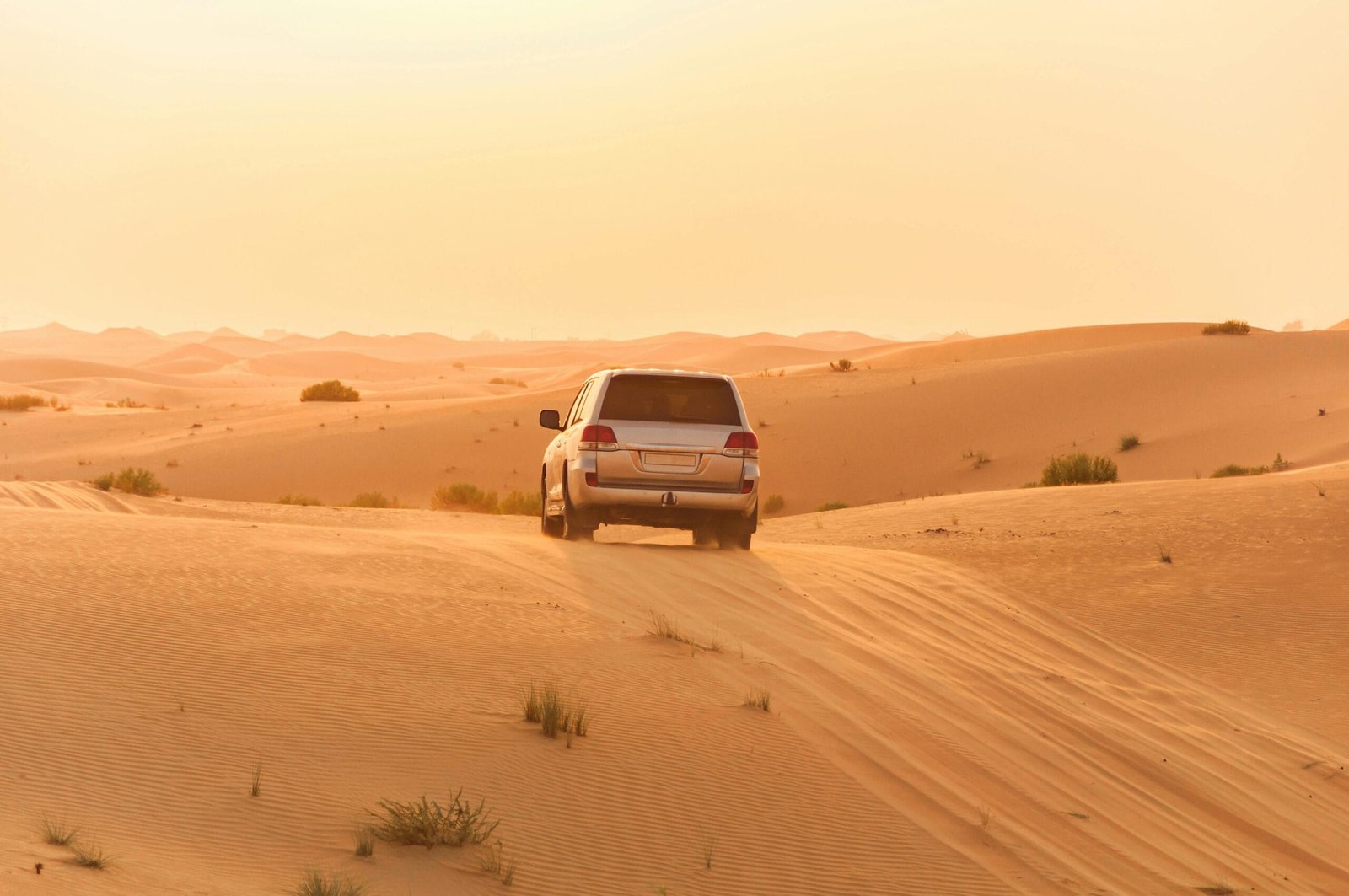 A white SUV driving through the sand dunes of the Arabian desert at sunset, capturing adventure and solitude.