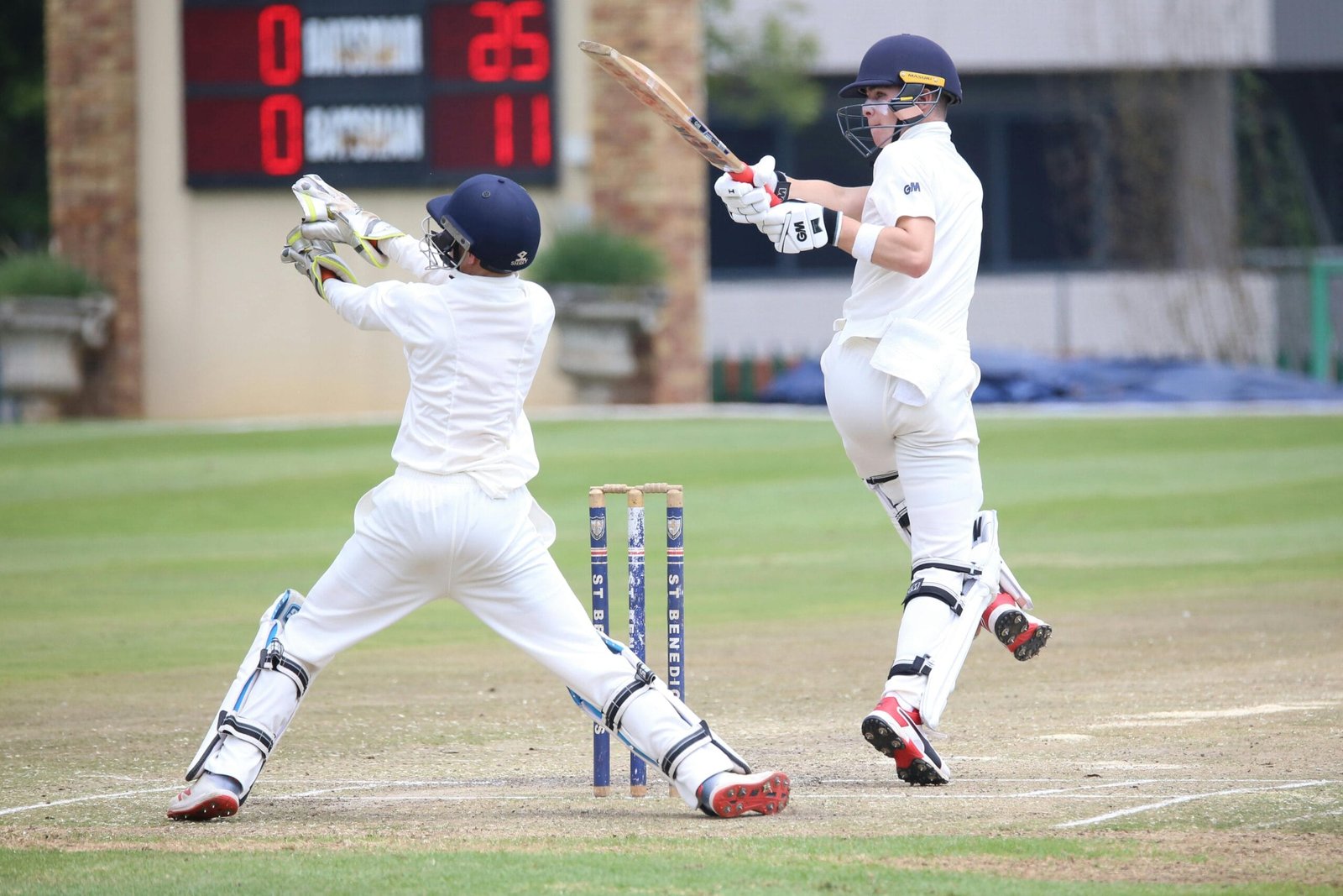 Dynamic cricket scene with batsman playing a shot and wicketkeeper in action.