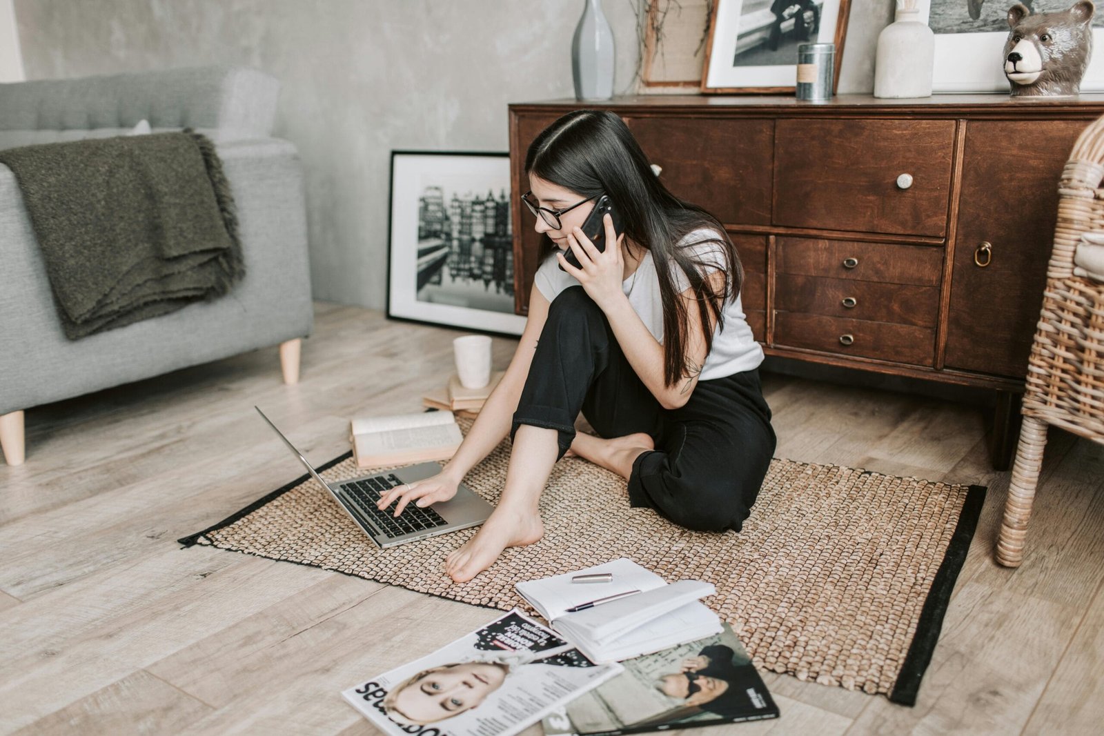 Young woman working from home, balancing laptop and phone calls on the floor.