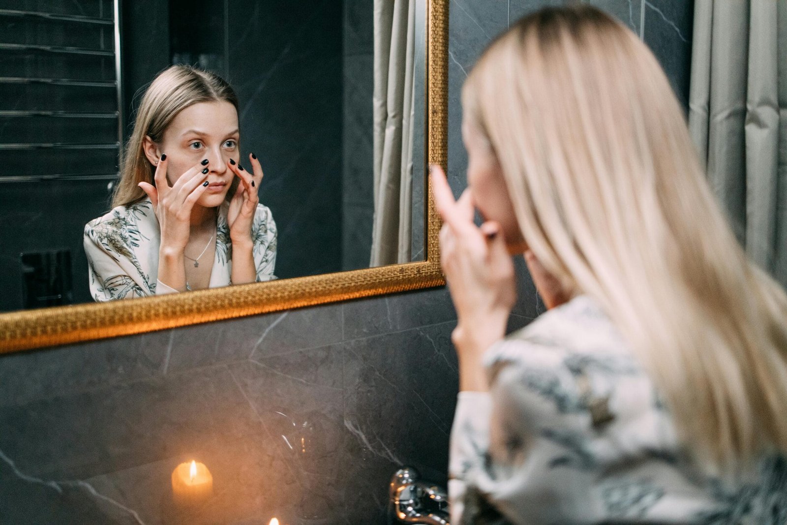 Woman applying a facial mask in a cozy bathroom setting with a candle-lit ambiance.