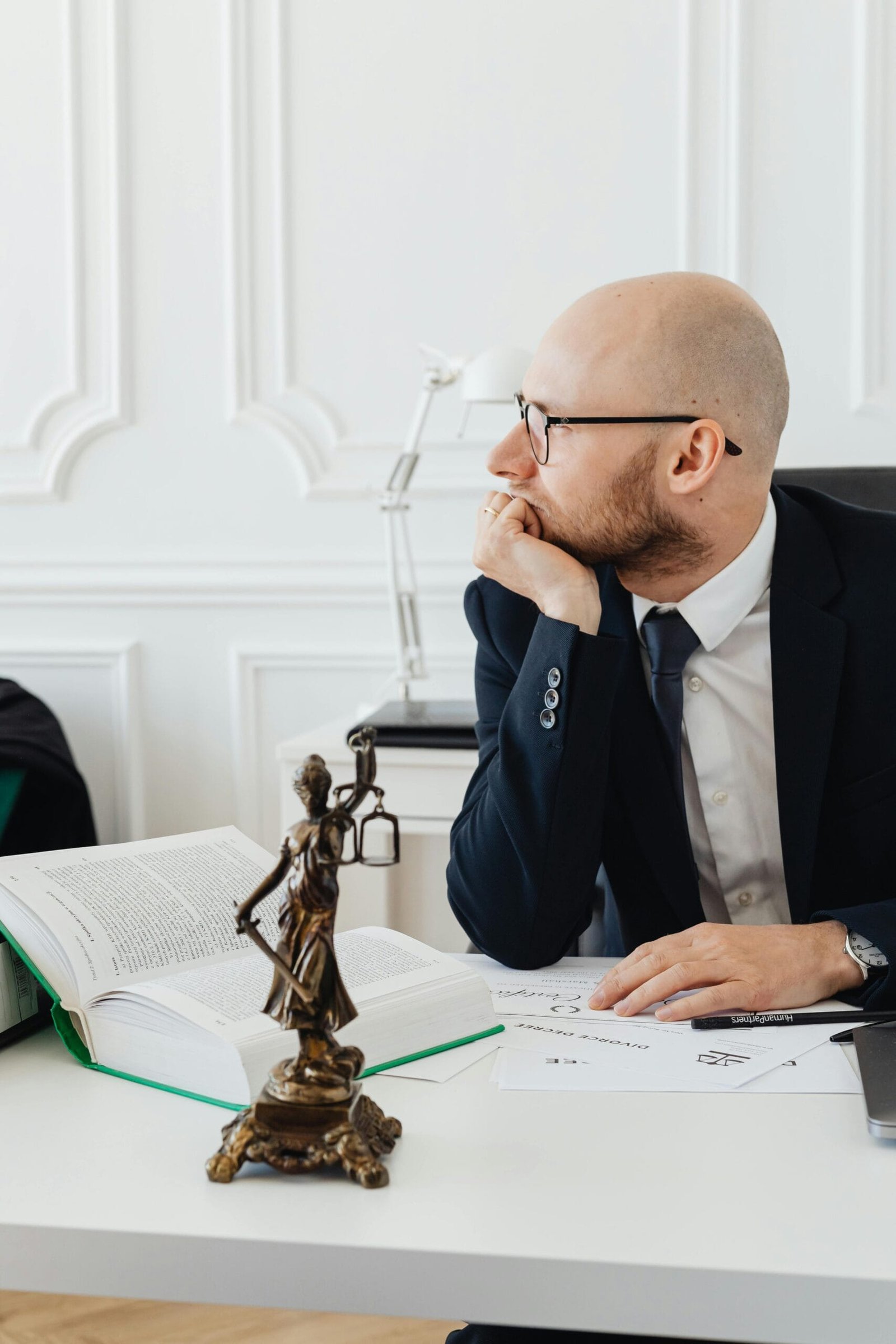 Lawyer in office with legal documents, deep in thought at desk with Temida statue.